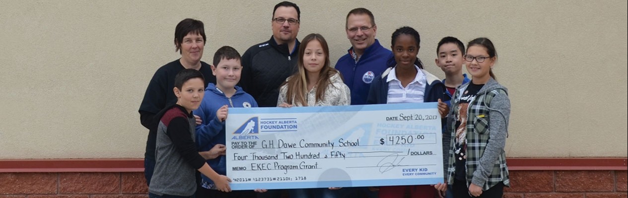 From left: G.H. Dawe Community School Principal Sue Carmichael, Executive Director of the Hockey Alberta Foundation Tim Leer, and Math/Gym teacher Daryl Puzey stand with a handful G.H. Dawe students as the Foundation presents a grant through the Every Kid